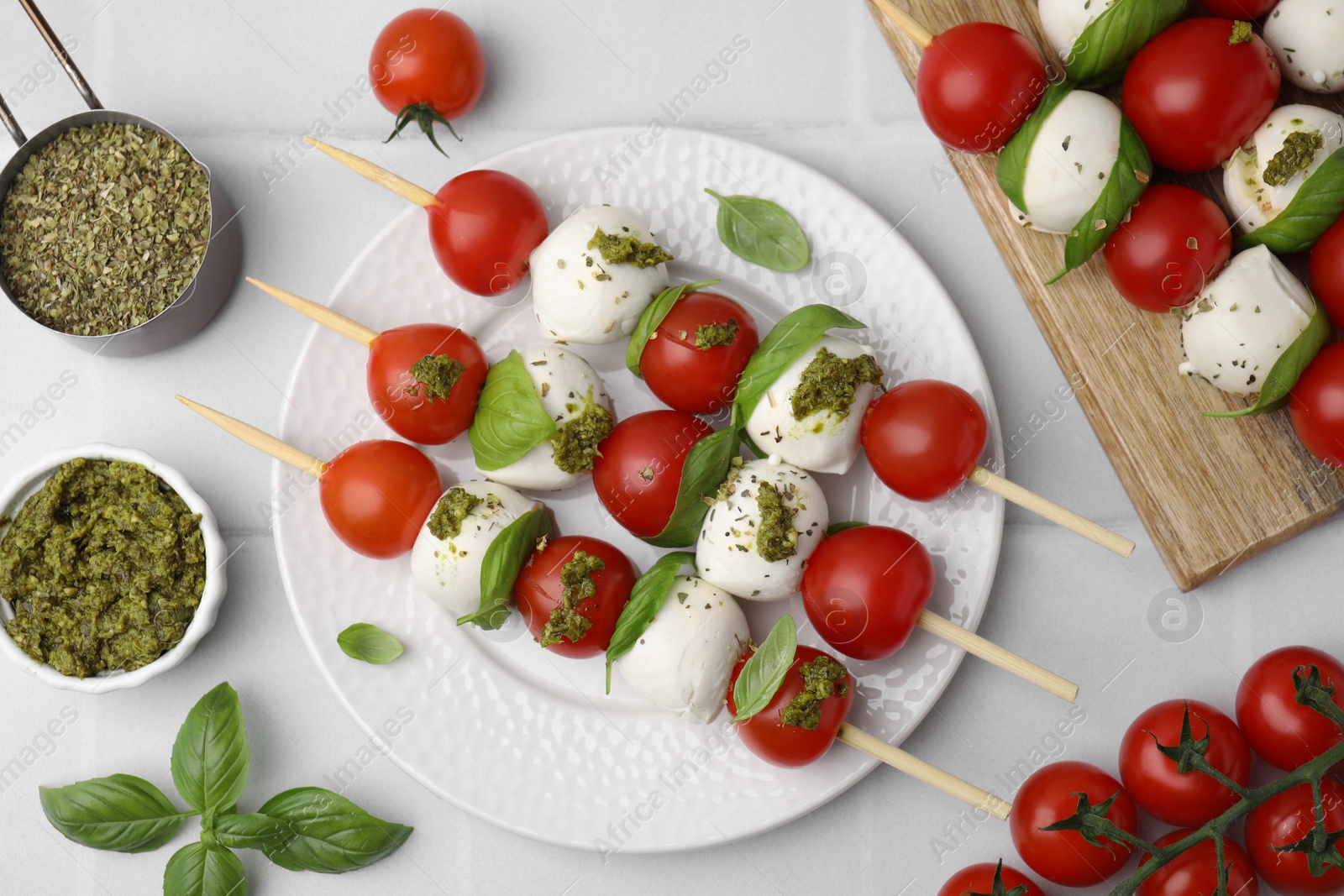 Photo of Caprese skewers with tomatoes, mozzarella balls and basil on white tiled table, flat lay