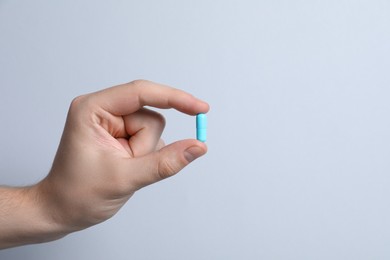 Photo of Man holding pill on light grey background, closeup. Space for text