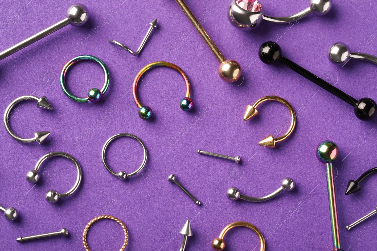 Photo of Stylish piercing jewelry on violet background, flat lay