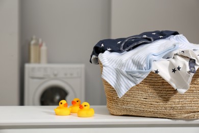 Photo of Laundry basket with baby clothes and rubber ducks on table in bathroom, closeup. Space for text