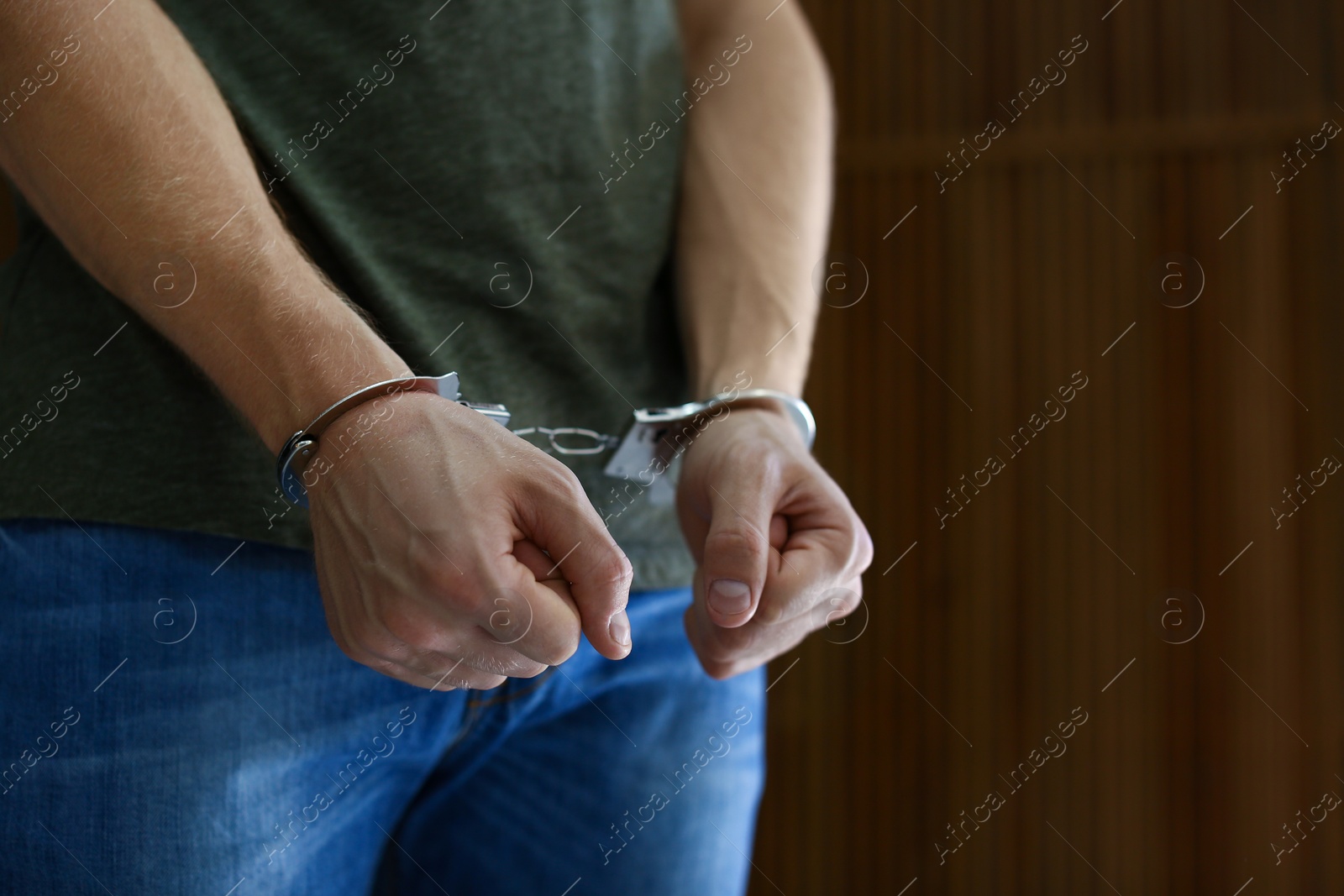 Photo of Man detained in handcuffs against blurred wooden background, space for text. Criminal law