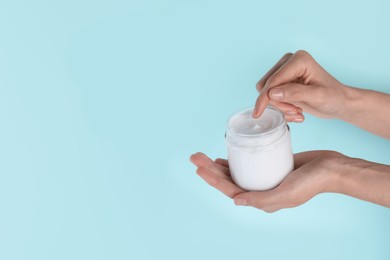 Photo of Woman holding jar of hand cream on turquoise background, closeup. Space for text
