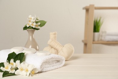 Photo of Beautiful jasmine flowers, towel, spa stones and herbal bags on white wooden table indoors, space for text