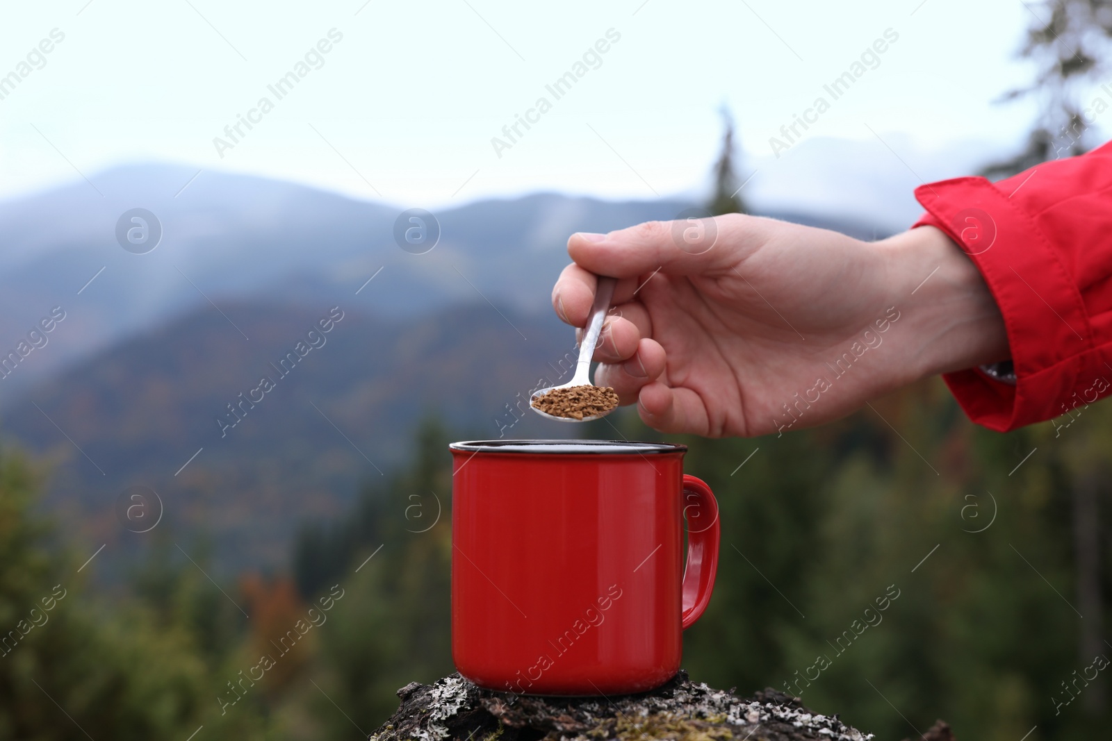 Photo of Woman pouring instant coffee into mug in mountains, closeup. Space for text