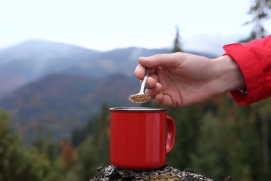 Photo of Woman pouring instant coffee into mug in mountains, closeup. Space for text