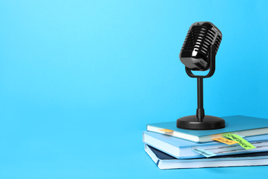 Photo of Retro microphone and notebooks on light blue background, space for text. Job interview