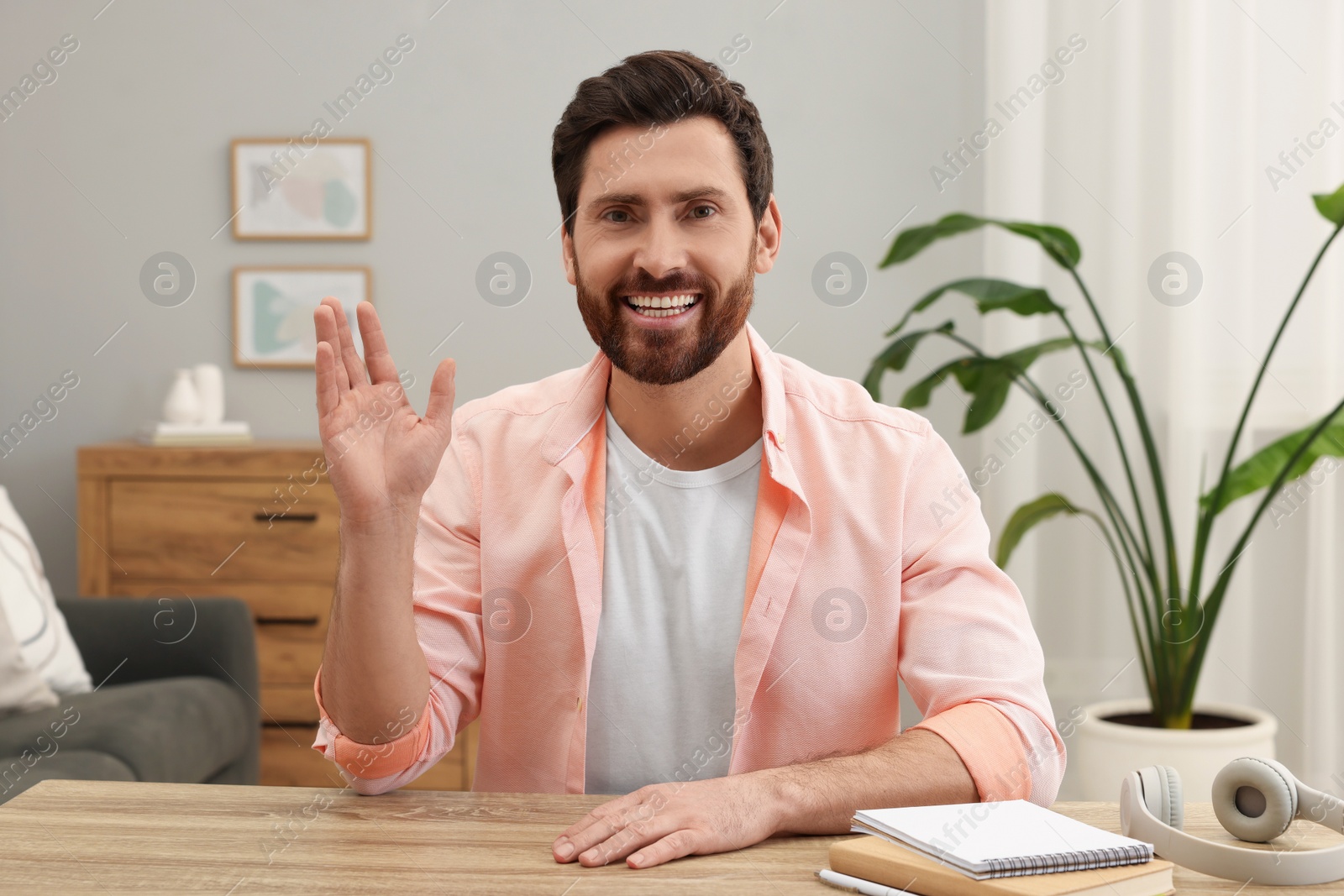 Photo of Stylish man greeting someone at wooden table indoors