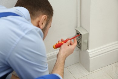 Photo of Electrician with screwdriver repairing power socket indoors, closeup