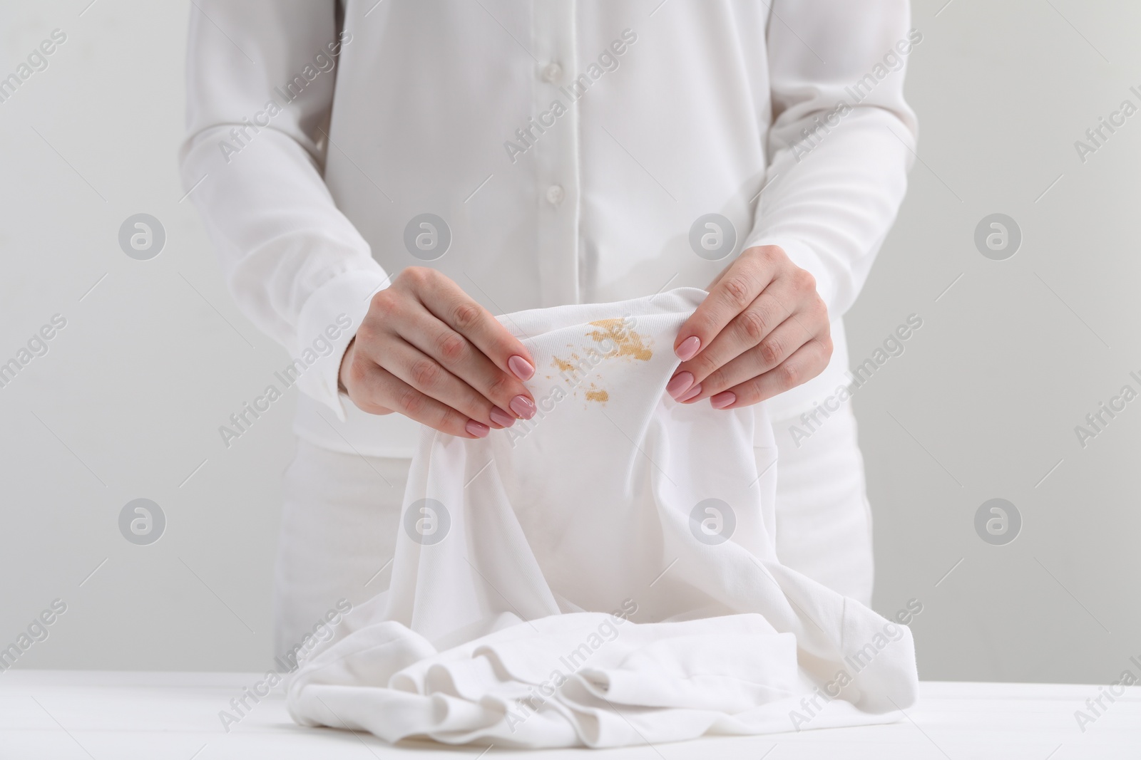 Photo of Woman holding shirt with stain at table against light background, closeup