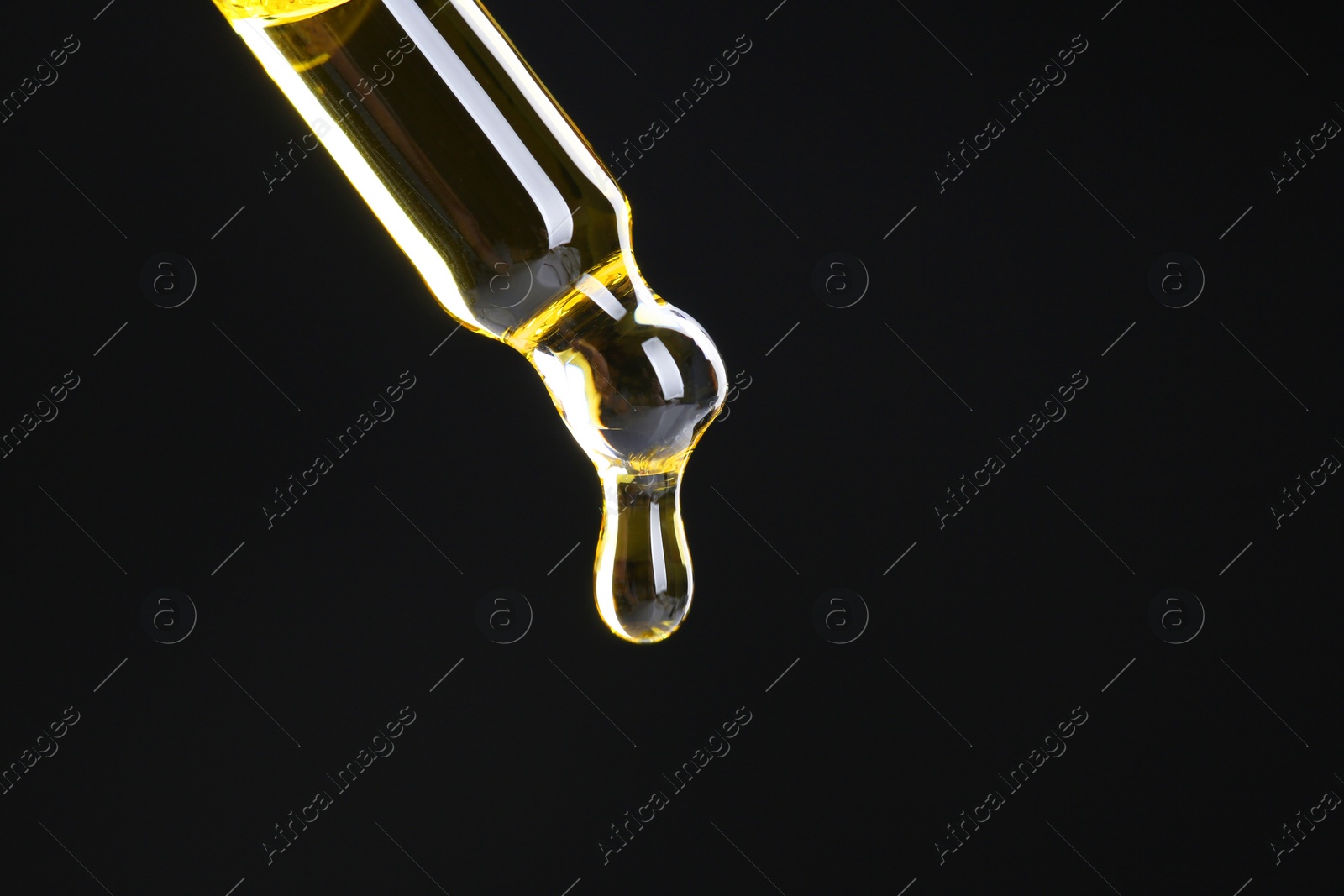 Photo of Dripping tincture from pipette on black background, closeup