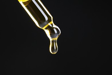 Photo of Dripping tincture from pipette on black background, closeup