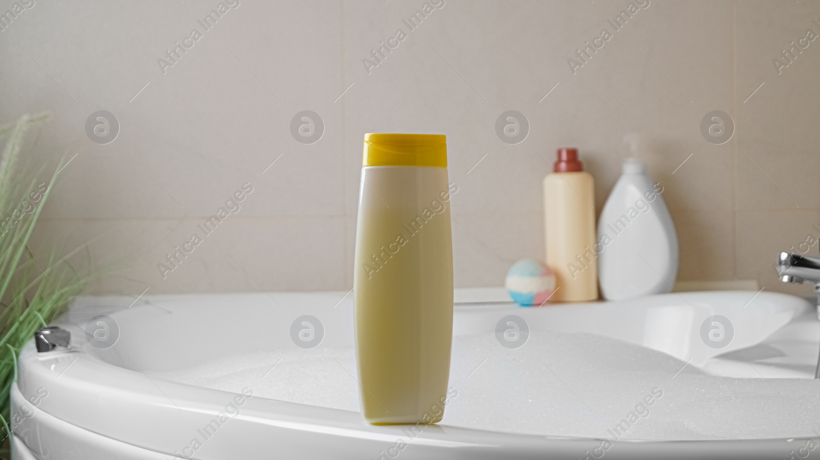 Beige bottle of bubble bath on tub indoors Photo of Beige bottle of bubble bath on tub indoors