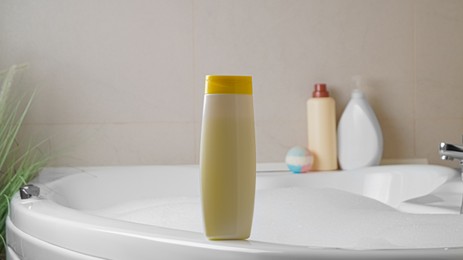 Photo of Beige bottle of bubble bath on tub indoors