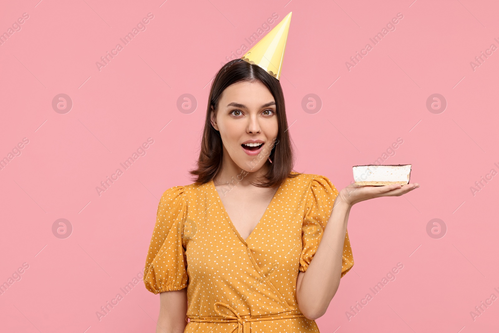 Photo of Surprised woman in party hat with cheesecake on pink background