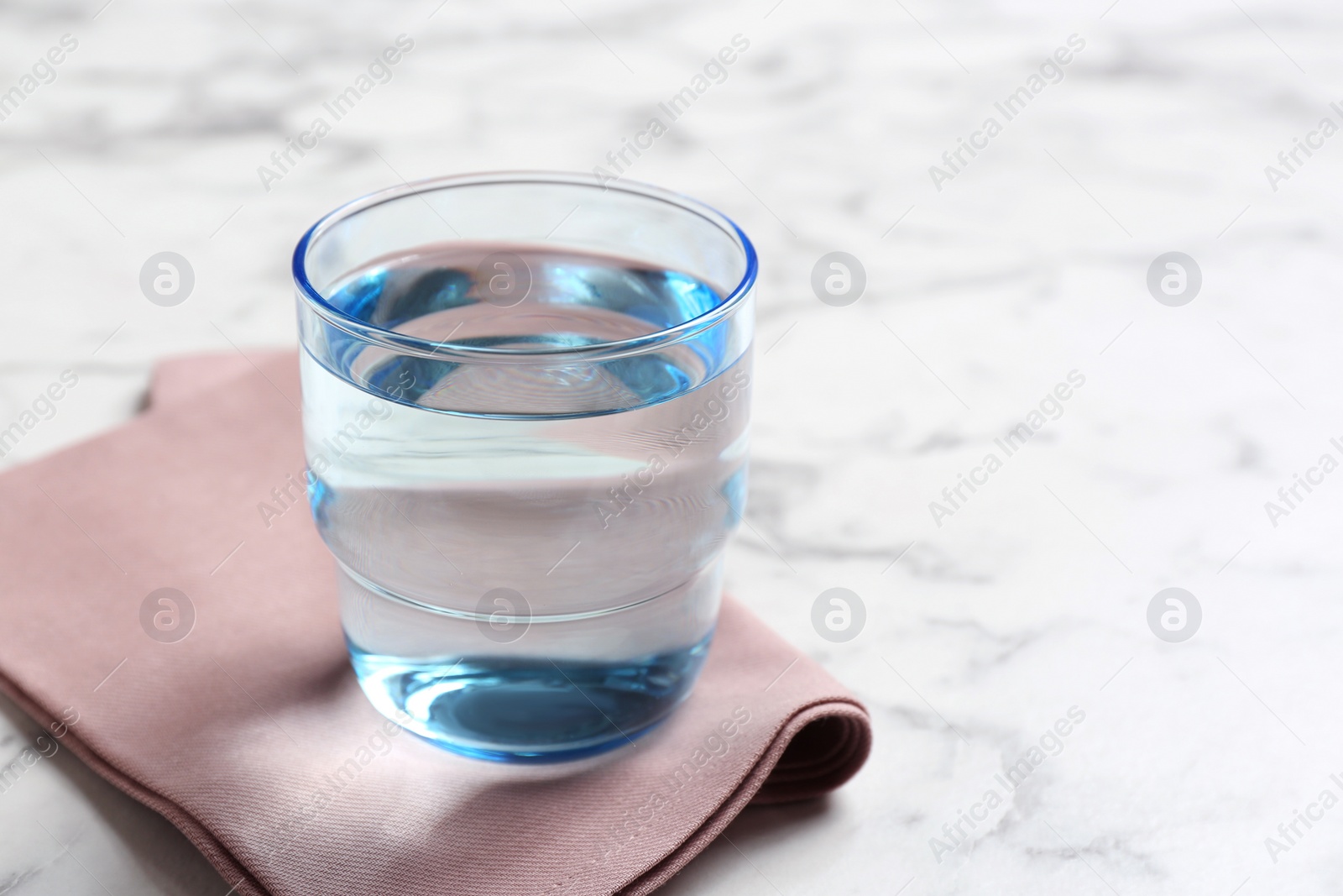 Photo of Glass with fresh water and napkin on marble table. Space for text