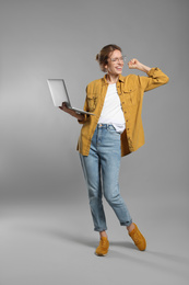 Full length portrait of emotional woman with modern laptop on grey background