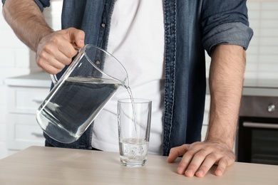 Photo of Man pouring water into glass at table, closeup