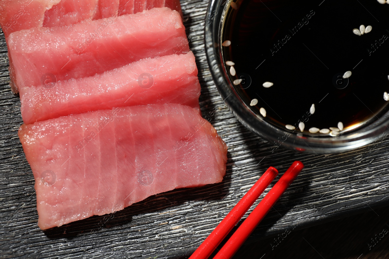 Photo of Tasty sashimi (pieces of fresh raw tuna) and soy sauce on black plate, flat lay