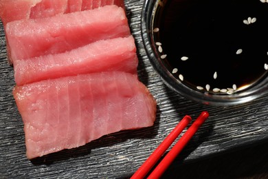 Photo of Tasty sashimi (pieces of fresh raw tuna) and soy sauce on black plate, flat lay