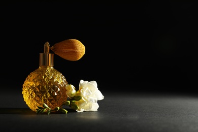 Photo of Vintage bottle of perfume and beautiful flower on black background, space for text
