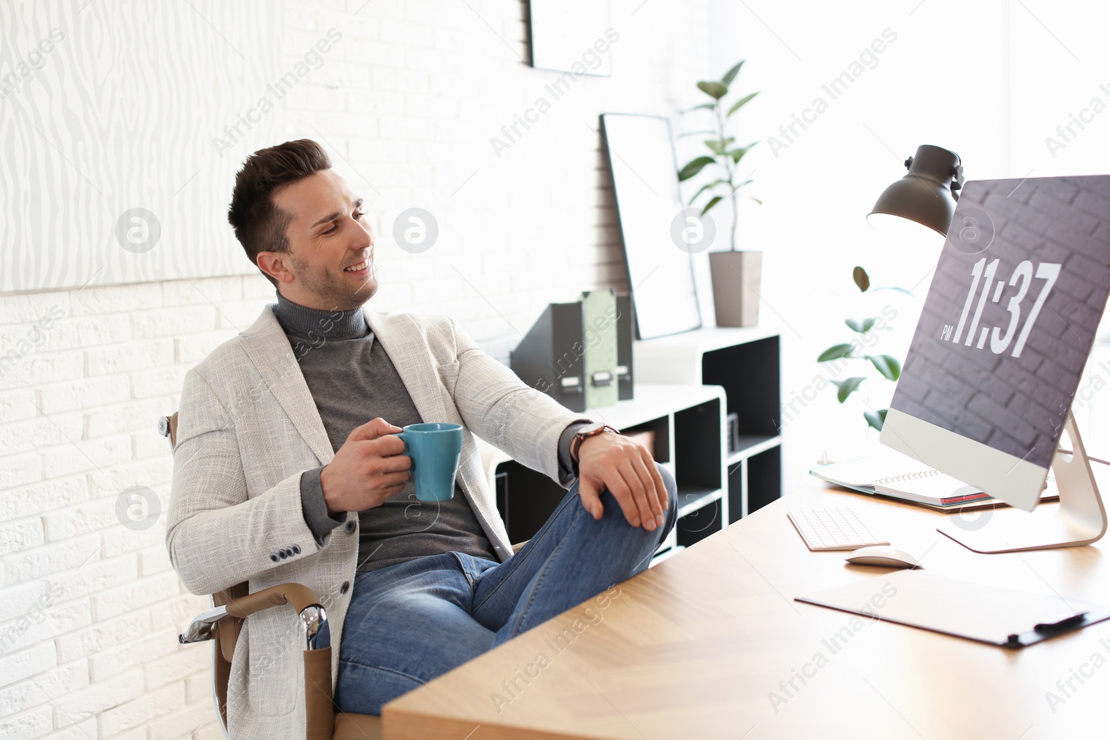 Photo of Young man with cup of drink relaxing at table in office during break