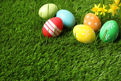 Photo of Colorful Easter eggs and narcissus flowers in green grass. Space for text