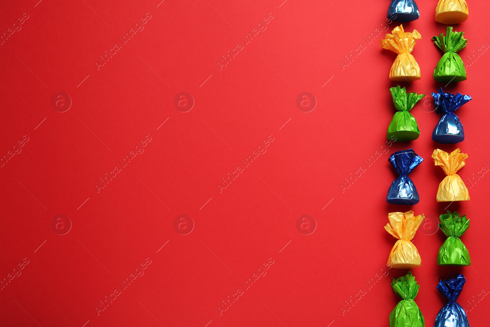 Photo of Many candies in colorful wrappers on red background, flat lay. Space for text