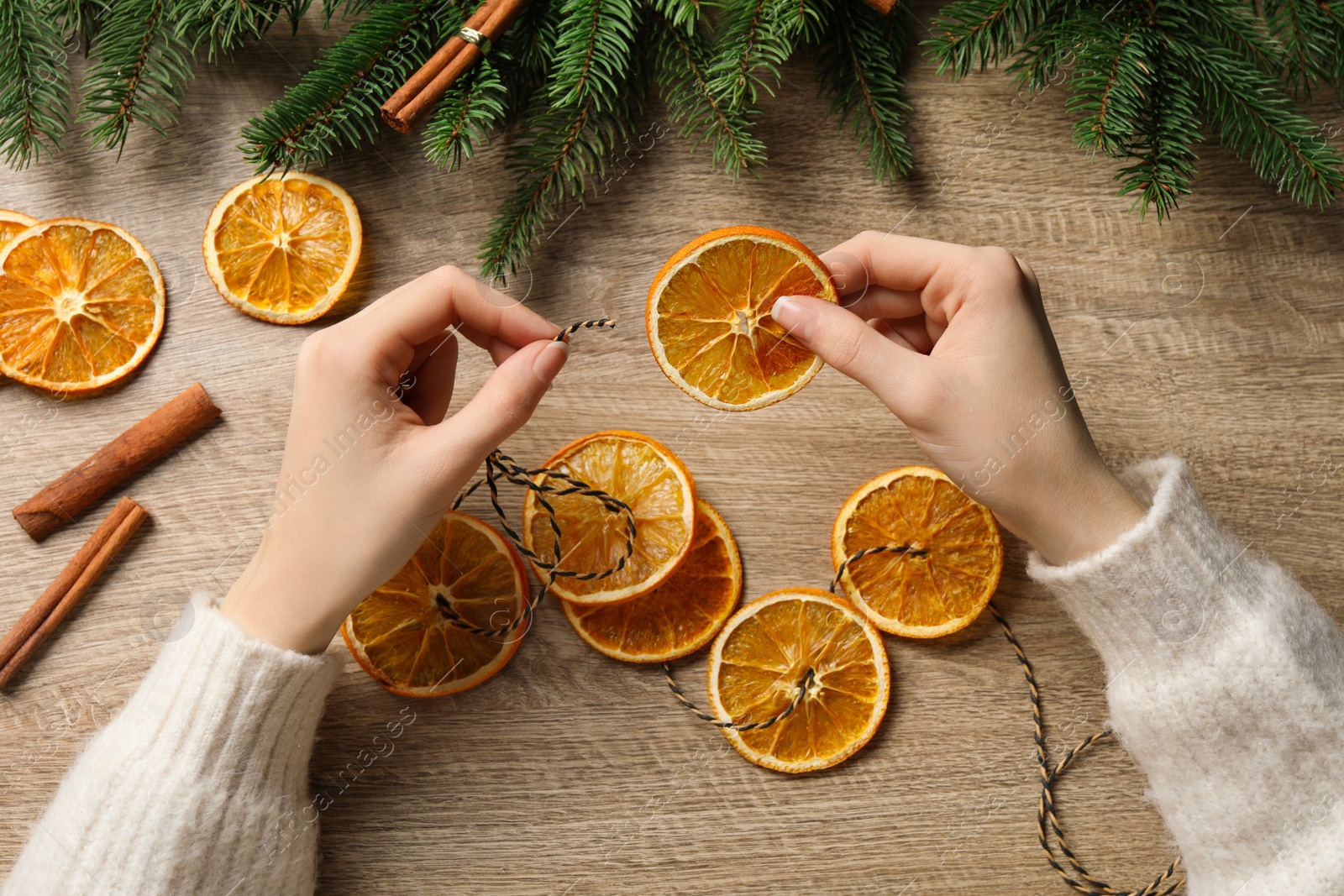 Photo of Woman making handmade garland from dry orange slices at wooden table, top view