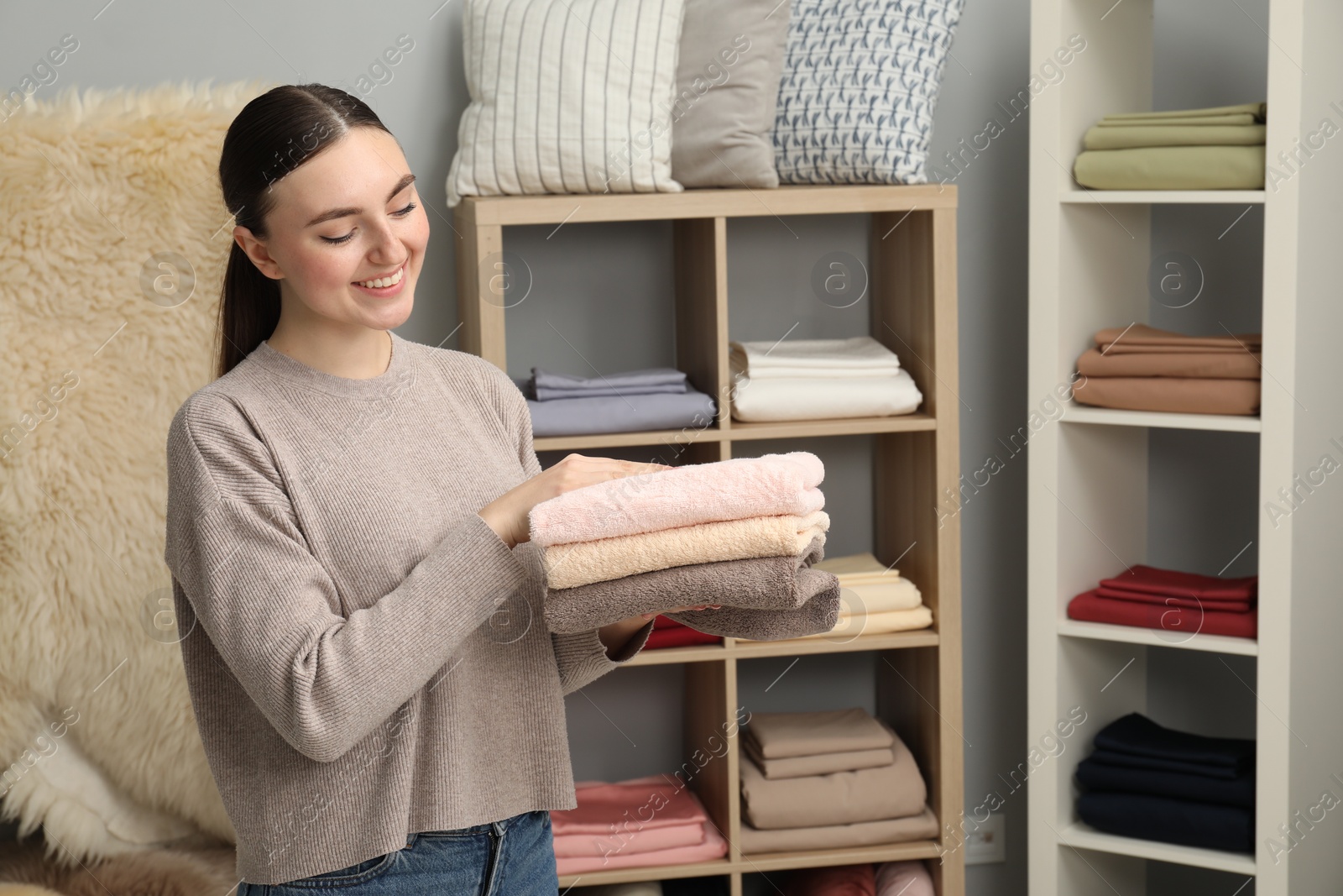 Photo of Smiling young woman holding stack of towels in home textiles store. Space for text