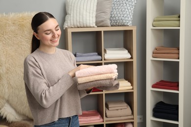 Smiling young woman holding stack of towels in home textiles store. Space for text