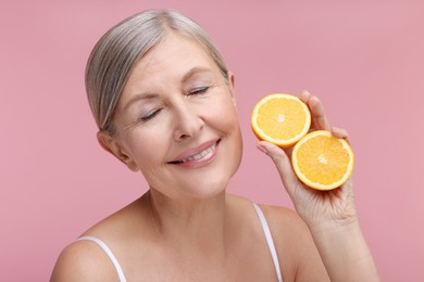 Photo of Beautiful woman with halves of orange rich in vitamin C on pink background