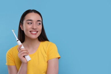 Photo of Happy young woman holding electric toothbrush on light blue background, space for text