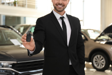 Photo of Salesman with key in modern car salon, closeup