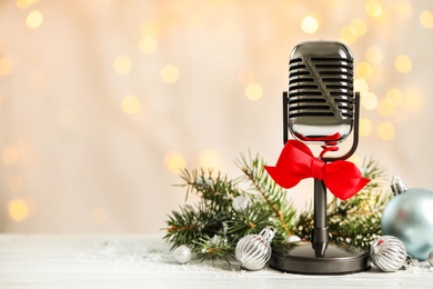 Photo of Microphone with red bow and decorations on white table against blurred lights, space for text. Christmas music