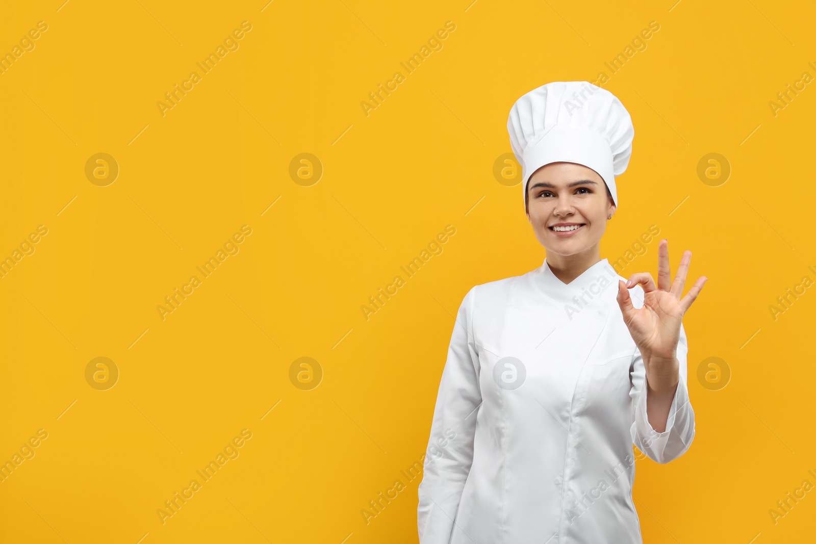 Photo of Happy female chef showing ok gesture on orange background. Space for text