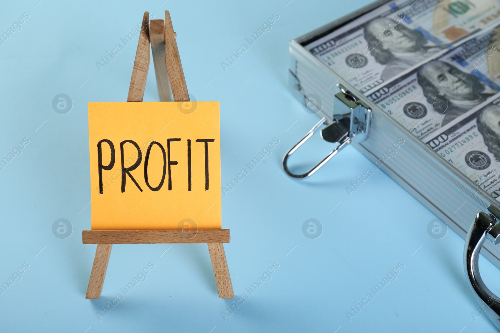 Photo of Economic profit. Easel with note and banknotes in briefcase on light blue background, closeup