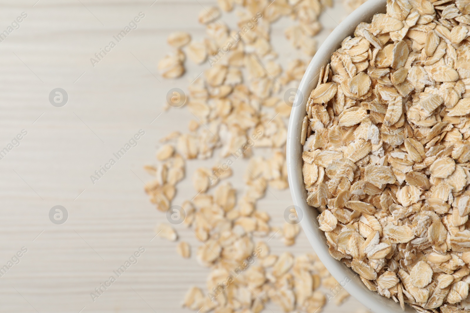 Photo of Bowl with oatmeal on white wooden table, top view. Space for text