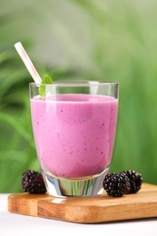 Photo of Delicious blackberry smoothie in glass and berries on white table