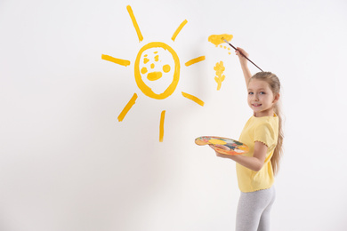 Little child painting sun on white wall indoors