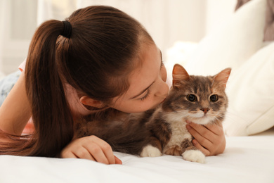 Photo of Cute little girl with cat lying on bed at home. First pet