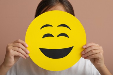 Photo of Little girl covering face with laughing emoji on pale pink background