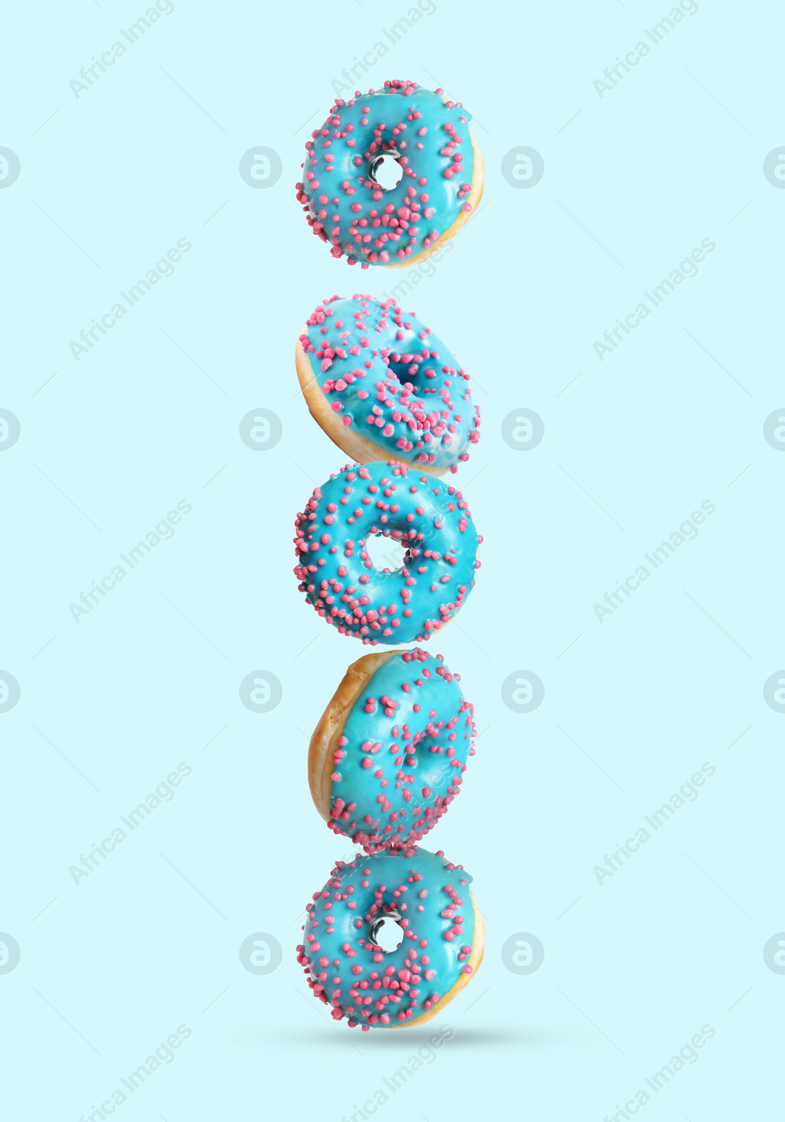 Image of Tasty donuts with sprinkles falling on light blue background