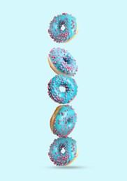 Image of Tasty donuts with sprinkles falling on light blue background
