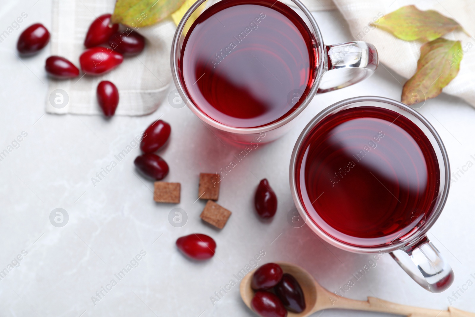 Photo of Glass cups of fresh dogwood tea, berries and sugar on light grey table, flat lay. Space for text