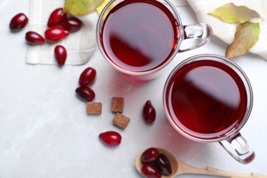 Glass cups of fresh dogwood tea, berries and sugar on light grey table, flat lay. Space for text