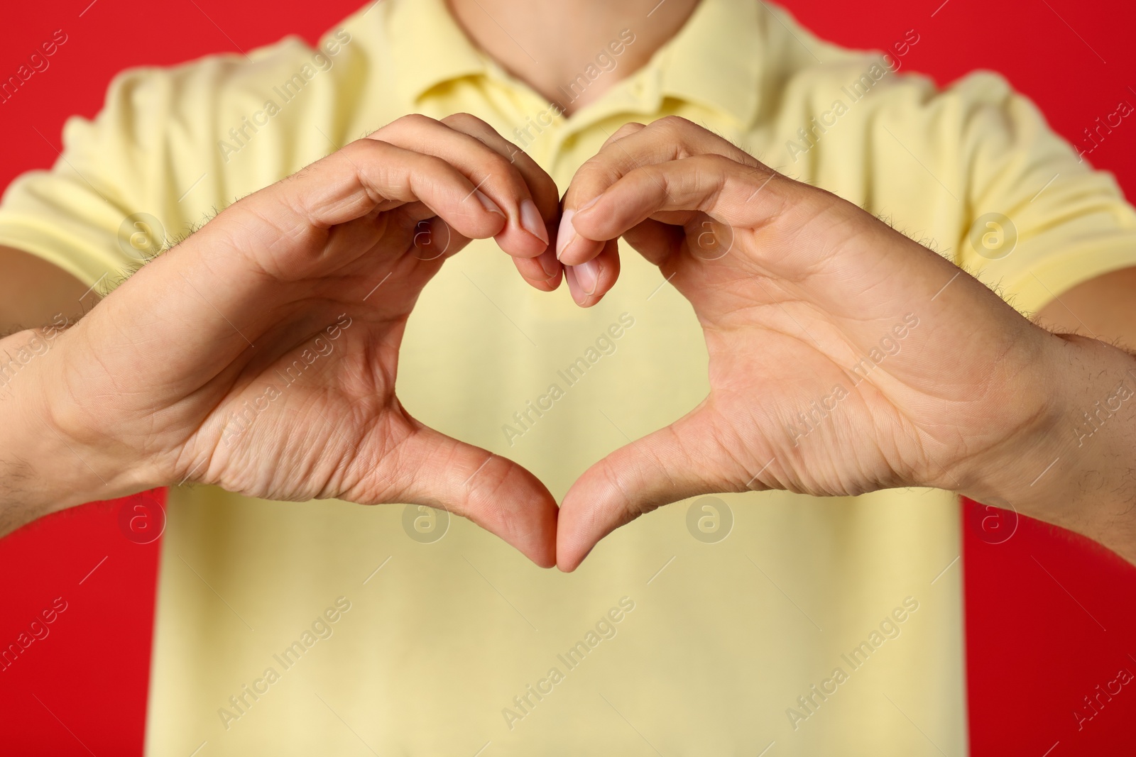 Photo of Man making heart with hands on red background, closeup