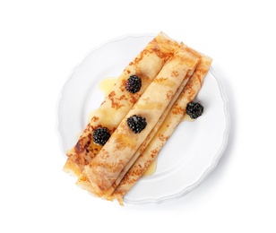 Photo of Tasty thin pancake rolls with blackberries on plate against white background, top view