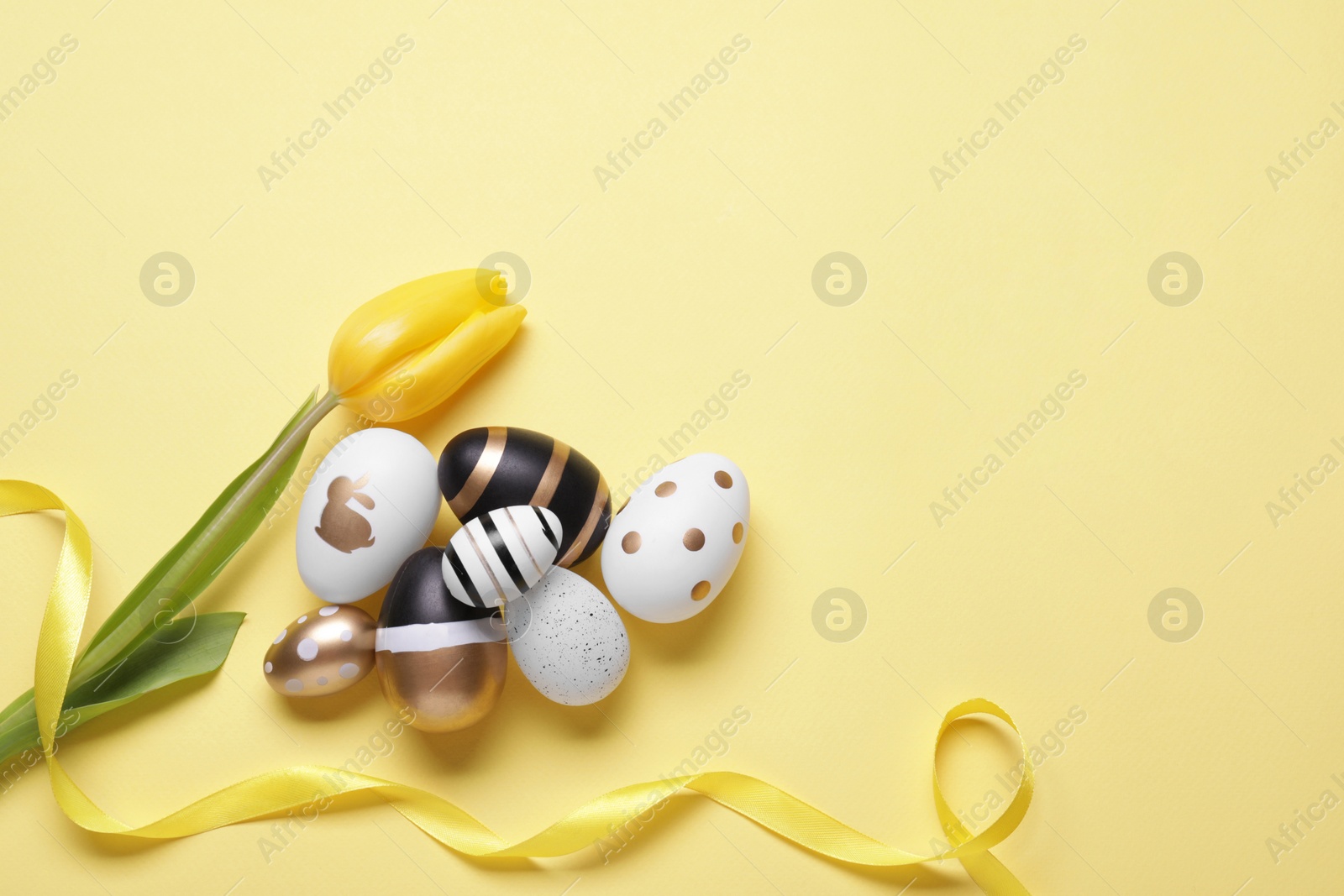 Photo of Flat lay composition with tulip and beautifully painted eggs on yellow background, space for text. Easter celebration