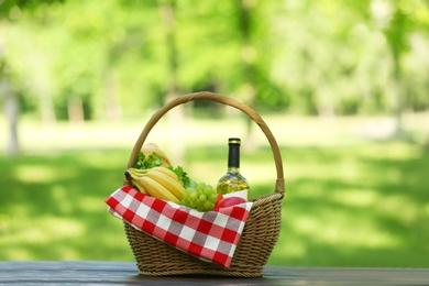 Wicker basket with blanket, wine and food on table in park. Summer picnic