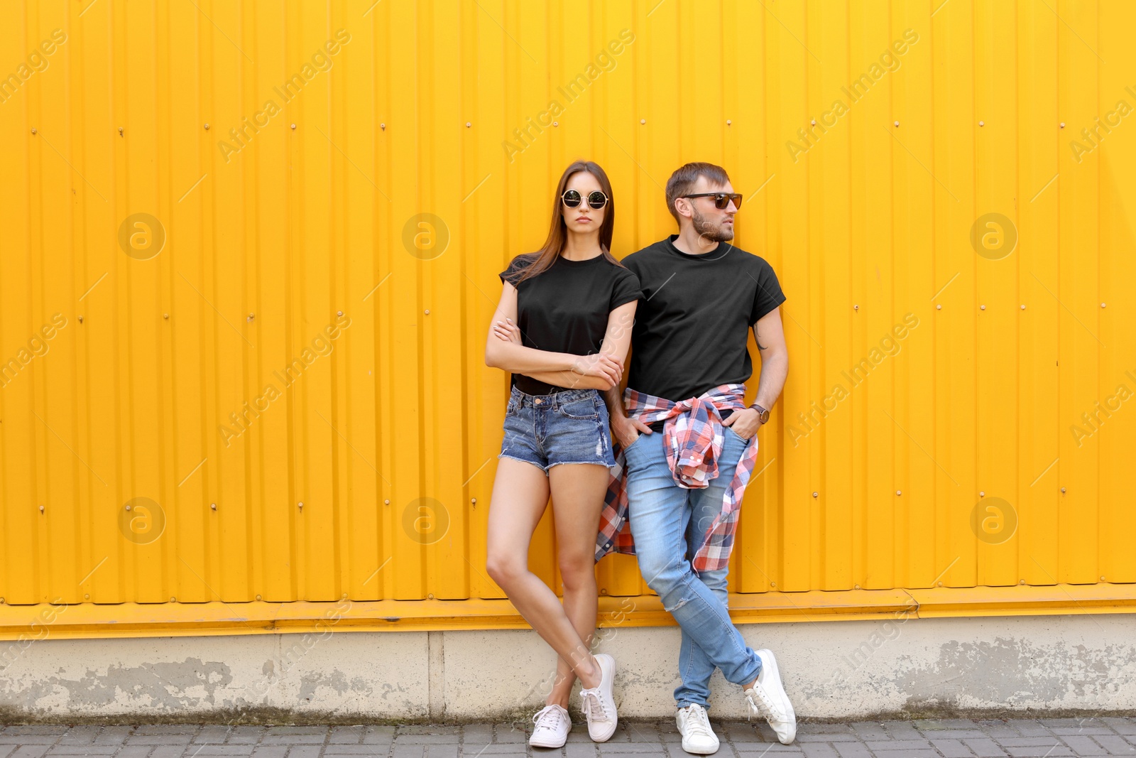 Photo of Young couple wearing black t-shirts near color wall on street